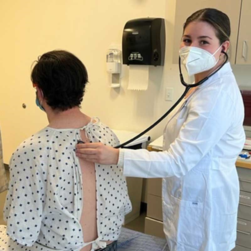 UMass Lowell nursing graduate student uses a stethoscope on a patient's back.