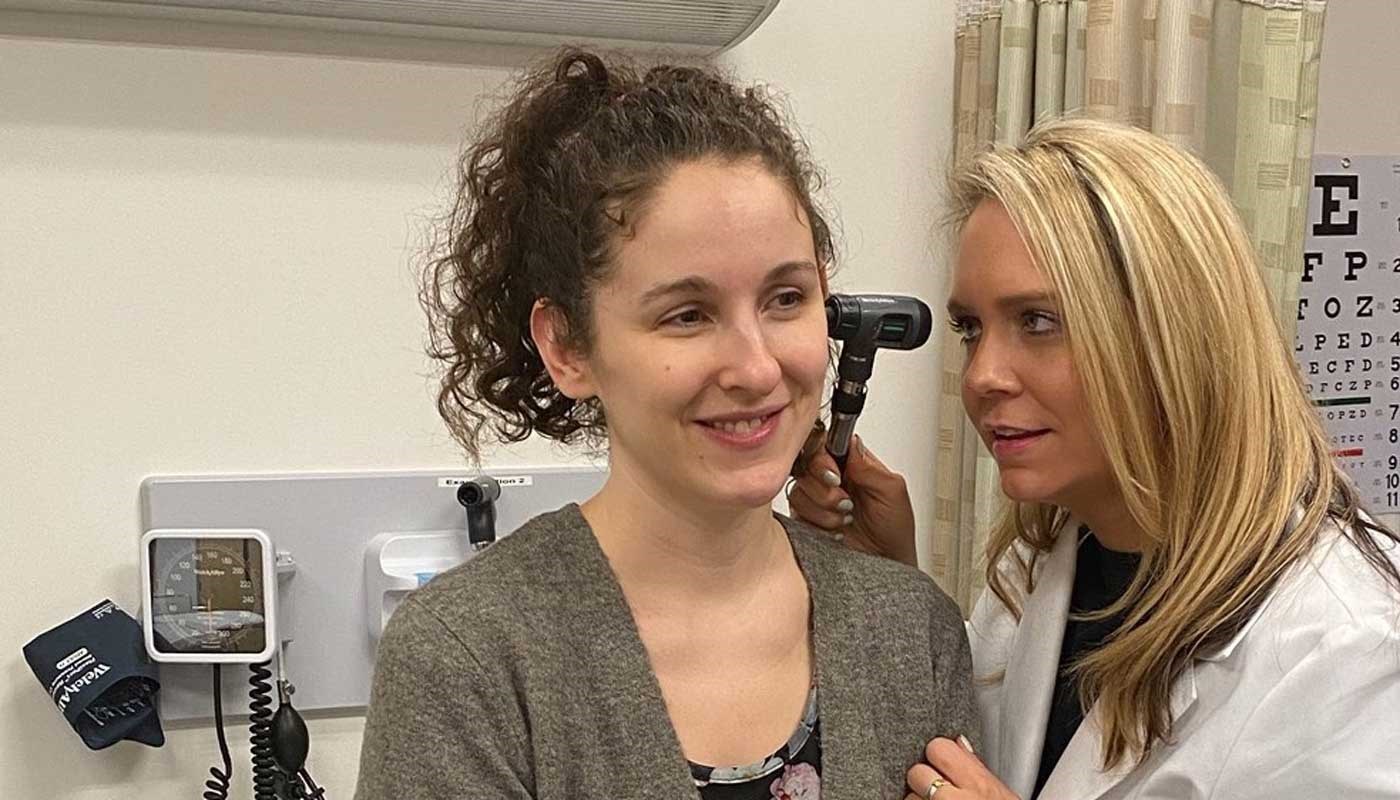 Nursing student uses a medical device to examine a patient's ear