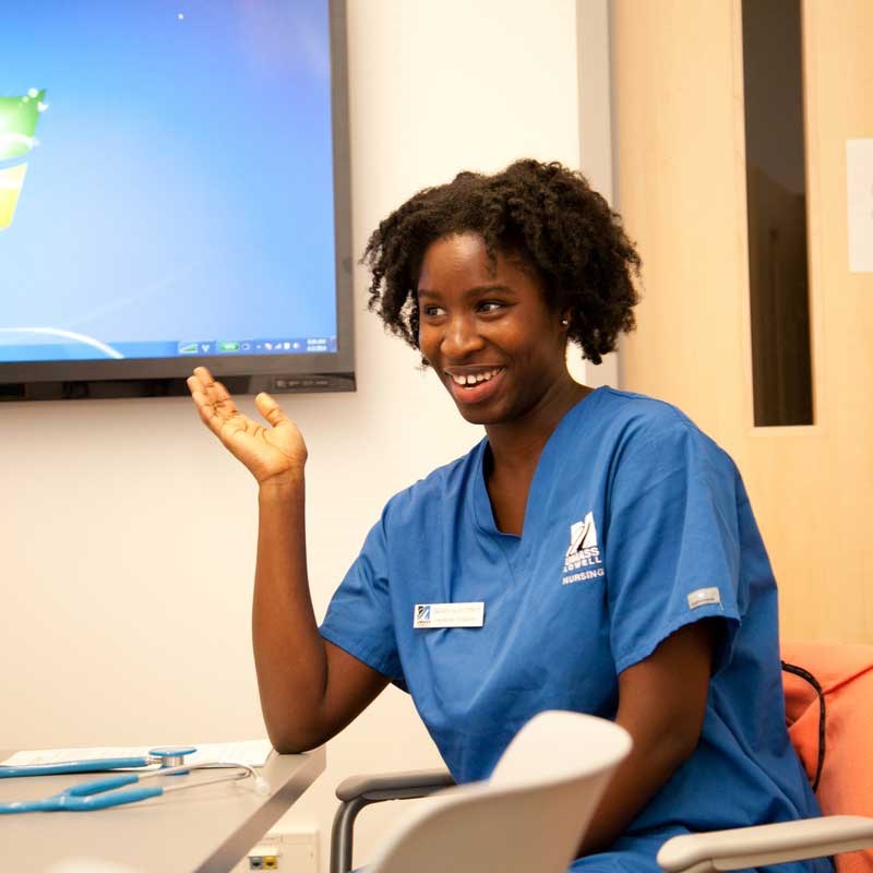 Nursing student wearing blue scrubs sits at a table in a UMass Lowell classroom