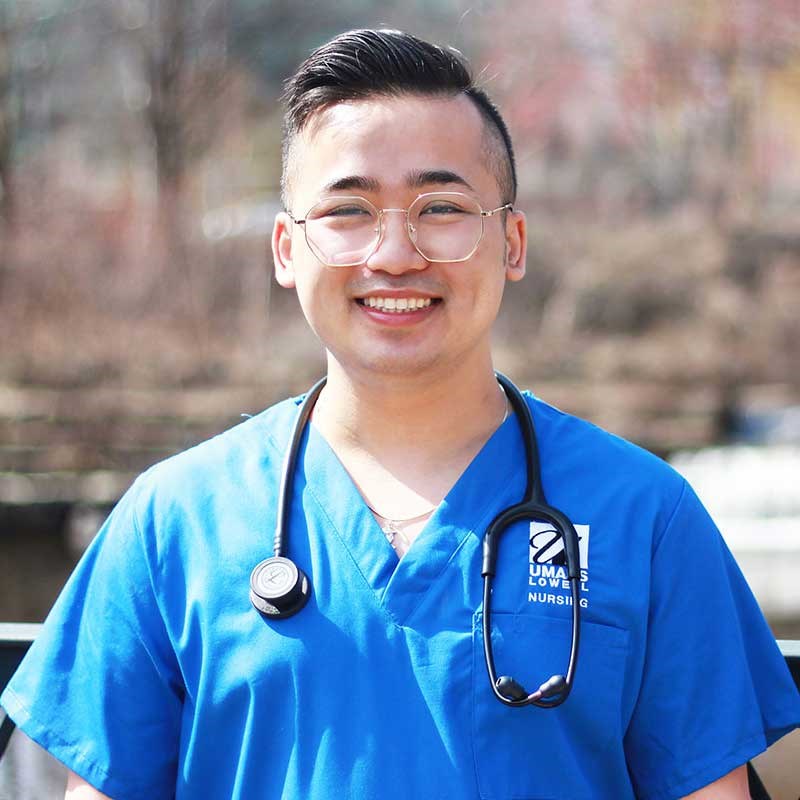 Nursing student poses wearing UMass Lowell blue scrubs and a stethoscope 