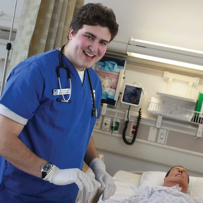 Nursing student wearing blue scrubs and gloves works in a UMass Lowell simulated hospital room