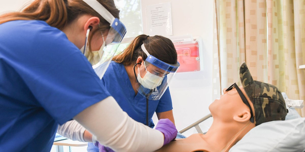 Two nursing students wearing face shields and masks working on dummy patient