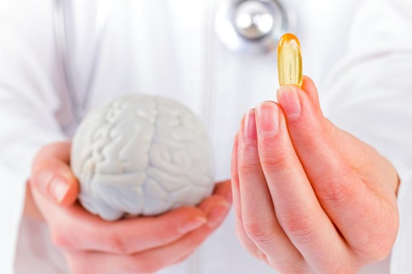 Doctor holding model of brain in one hand and omega-3 capsule in other