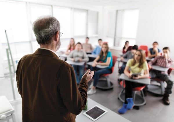 An older teacher faces his students in a classroom