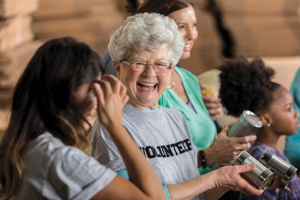 Older woman smiling, holding canned goods wearing a "volunteer" t-shirt