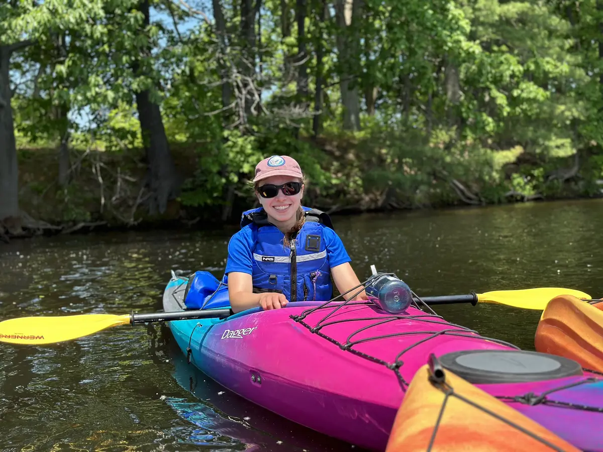A person wearing sunglasses and a hat floats in a kayak on a bright sunny day.