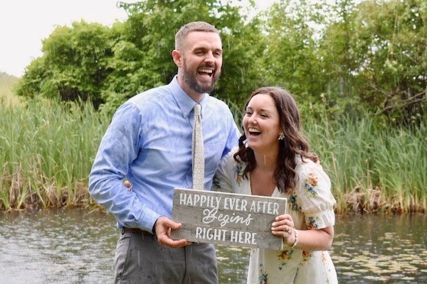 Justin Lawler and Devonne Sutton laugh while holding a wedding sign