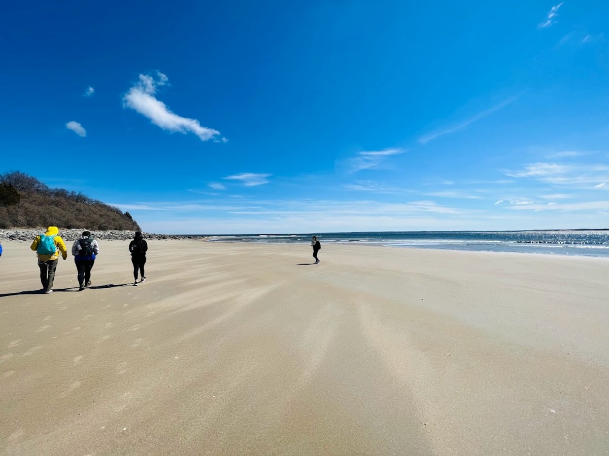 a group of people walk on a flat beach by the ocean with a blue sky above