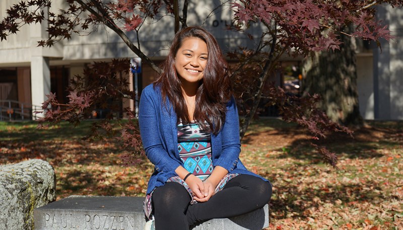 UMass Lowell student and tour guide Patrice Olivar sitting on a bench outside on South Campus