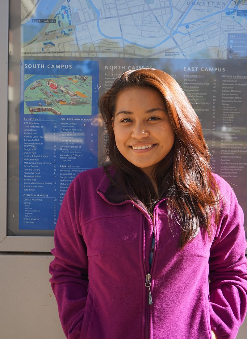 UMass Lowell student and tour guide Patrice Olivar standing in front of a campus map