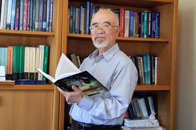 Paul Song in front of a bookshelf holding an open book on space