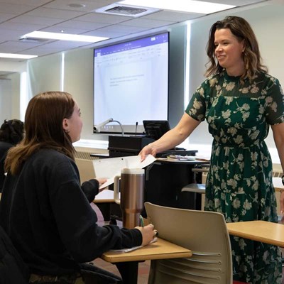 Professor hands a paper to a student in a philosophy classroom at UMass Lowell