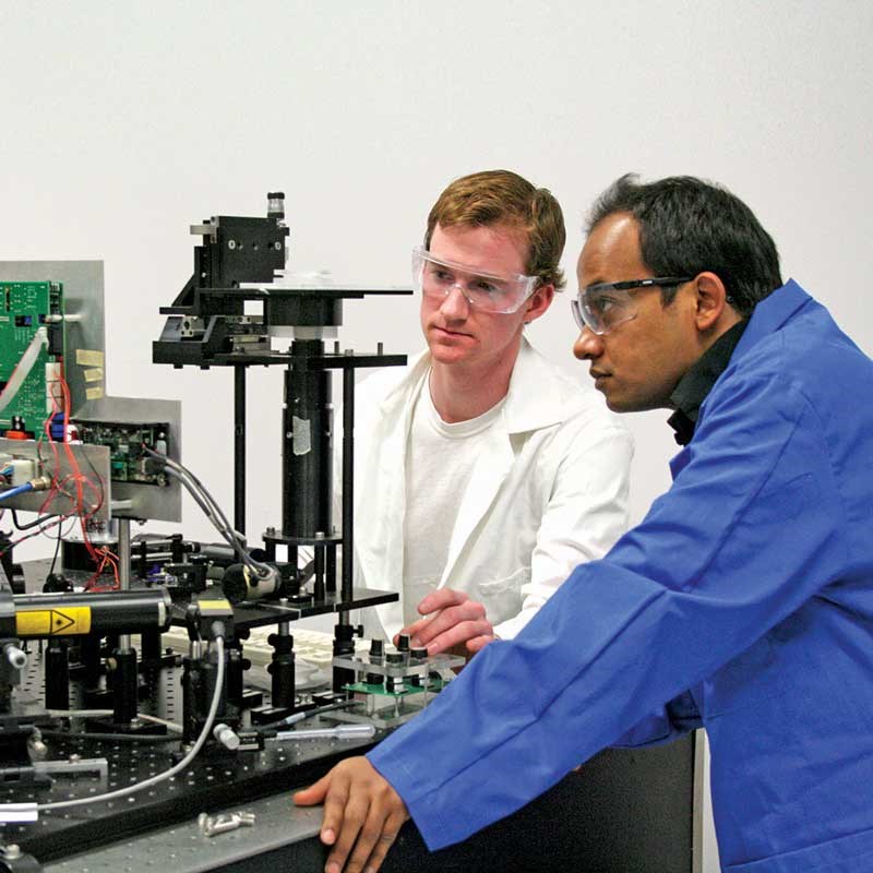 Two UMass Lowell physics students look at equipment in a classroom.
