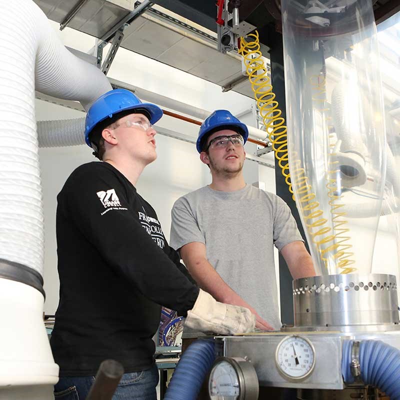 Two students wearing hard hats in a plastics recycling center at UMass Lowell