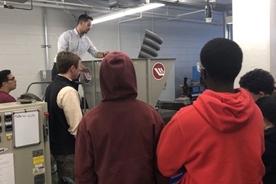 Students watch as man puts plastic into a shredder