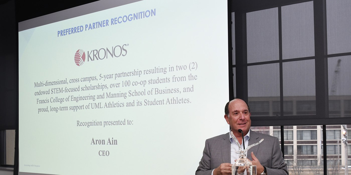 Kronos CEO Aron Ain in front of a presentation screen.