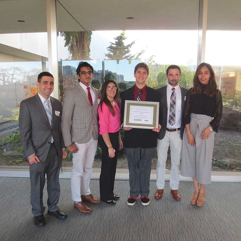 Economics students from UMass Lowell stand in a group with one student holding a framed certificate
