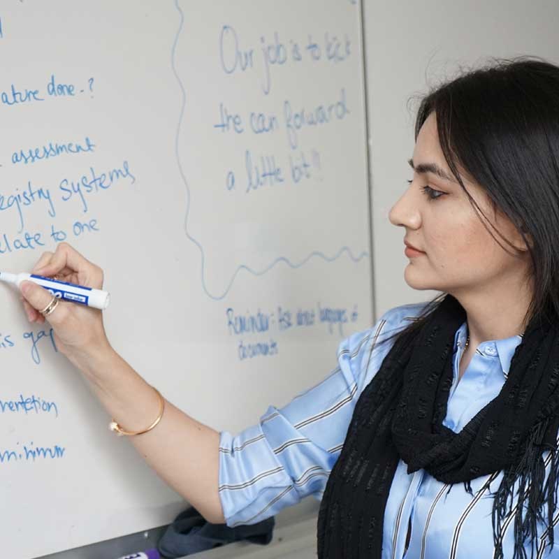 Qurat Ann writes on a whiteboard with a blue marker