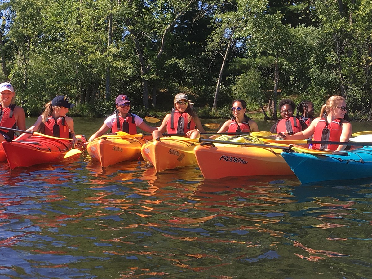RAMP group take some time out kayaking on the merrimack river during a sunny evening.  They are on the water in bright orange kayaks and look absolutely thrilled to be out of a classroom 