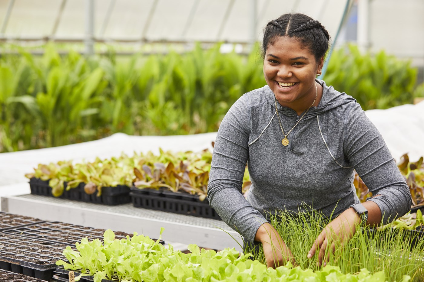 Young woman smiles as she tends to plants in greenhouse