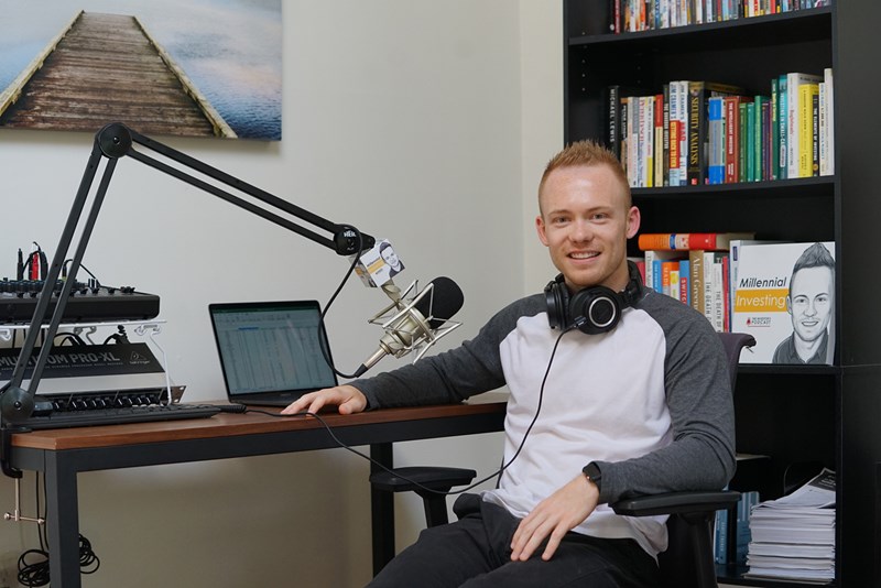 Robert Leonard sits at a laptop and microphone with headphones around his neck ready to record his podcast, "Millennial Investing"