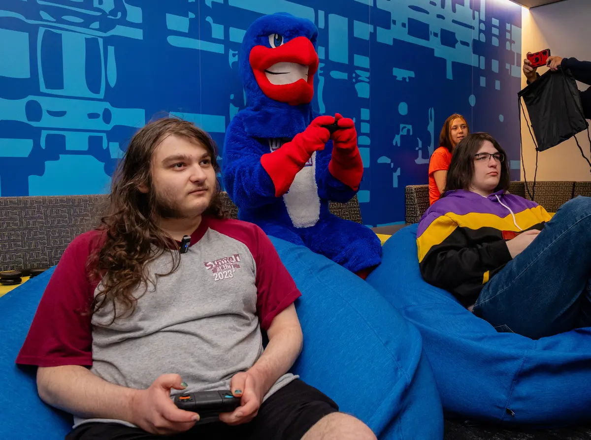 UMass Lowell mascot, Rowdy the River Hawk, plays video game with students at Rowdy's E-Sports Arena.