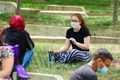 Socially distanced students in masks sit in the grass on campus