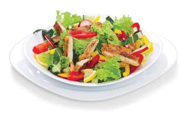 A salad with lettuce, chicken and yellow and red peppers on a white salad plate