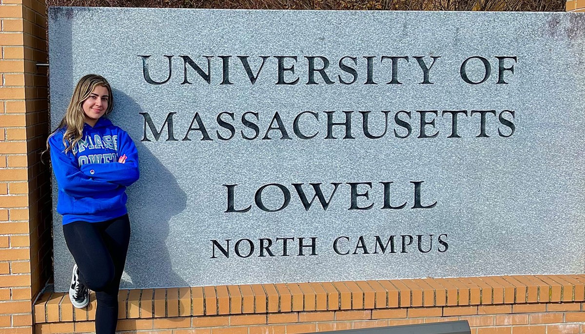 Sara is standing against the north campus sign at UMass Lowell