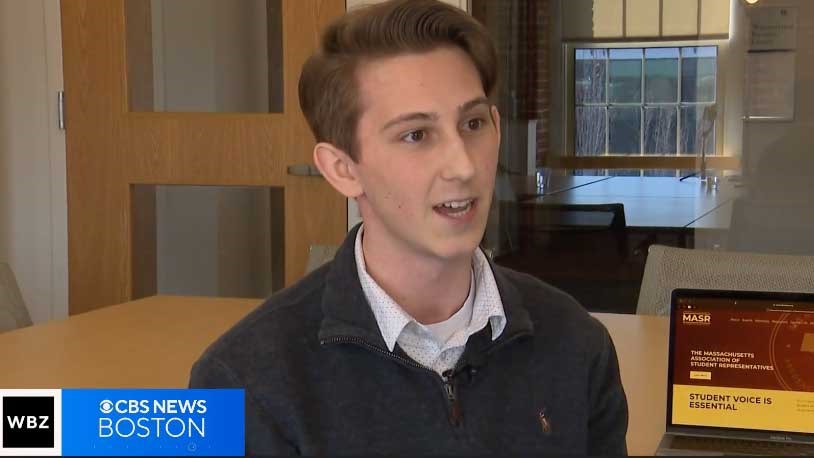 Sean Simonini being interviewed on WBZ CBS News with a laptop in the background showing a screen with the words "MASR, The Massachusetts Association of Student Representatives, Student Voice Is Essential."