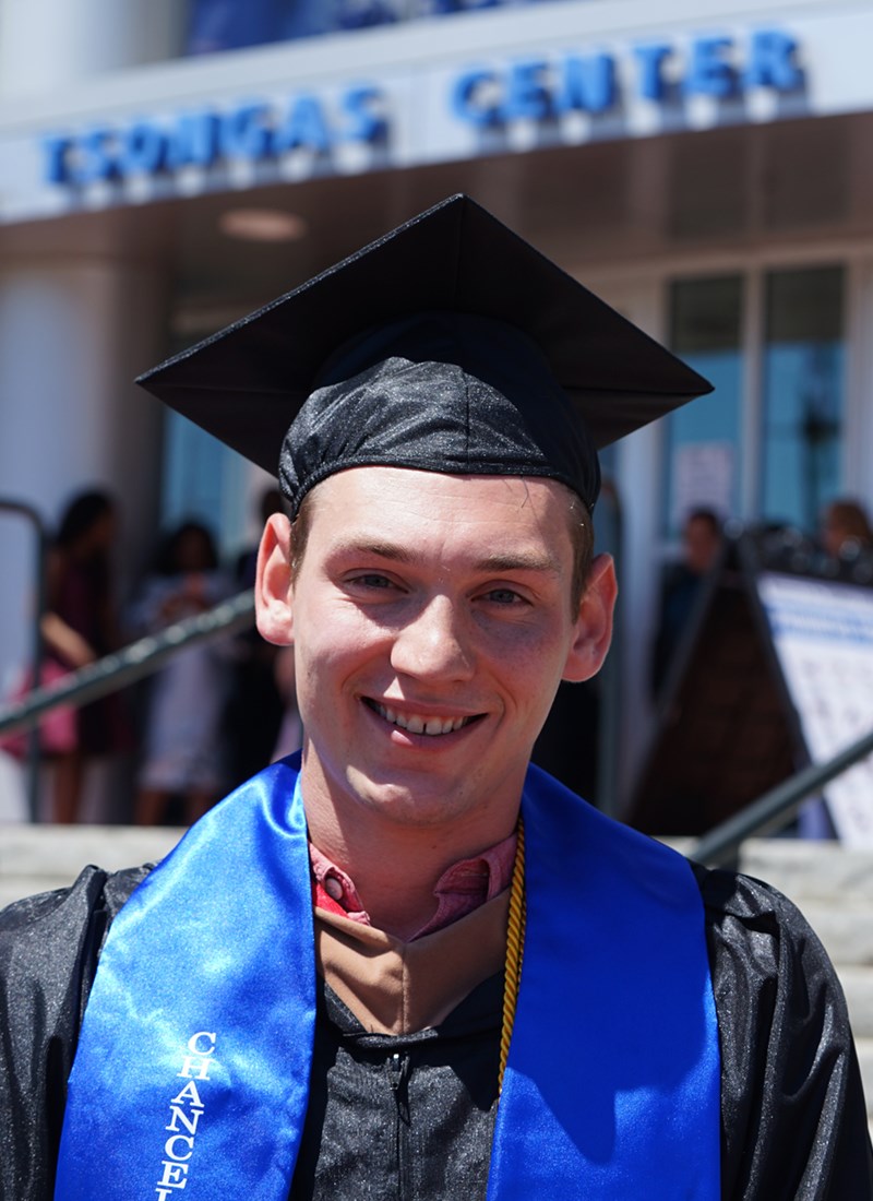 headshot of Sean Flaherty in cap and gown outside of the Tsongas Center after UMass Lowell's 2019 Commencement