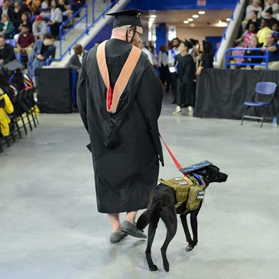 Graduate walks with his black Labrador during Commencement