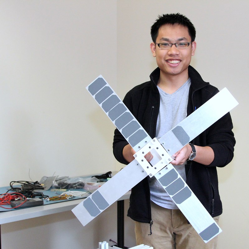 Simthyrearch Dy poses holding a scale model of SPACE HAUC, UMass Lowell’s first student-built satellite