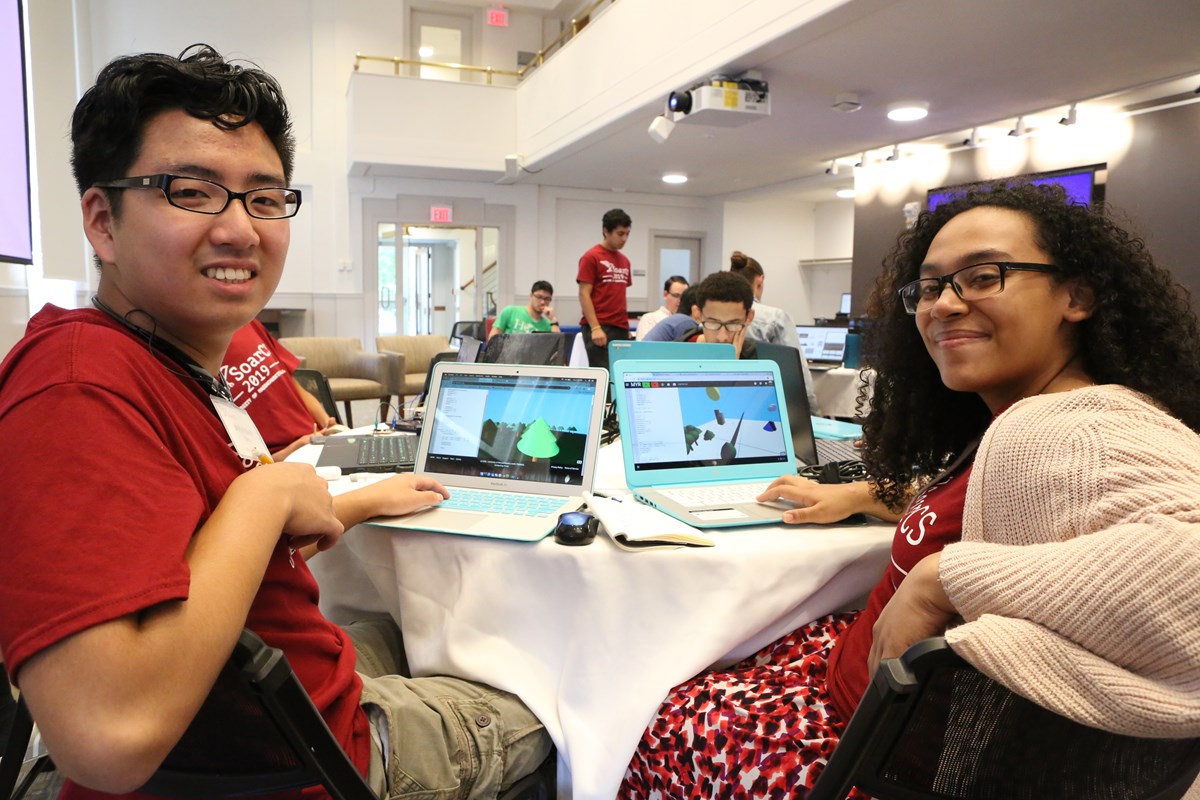 Two students sit at table with laptops open