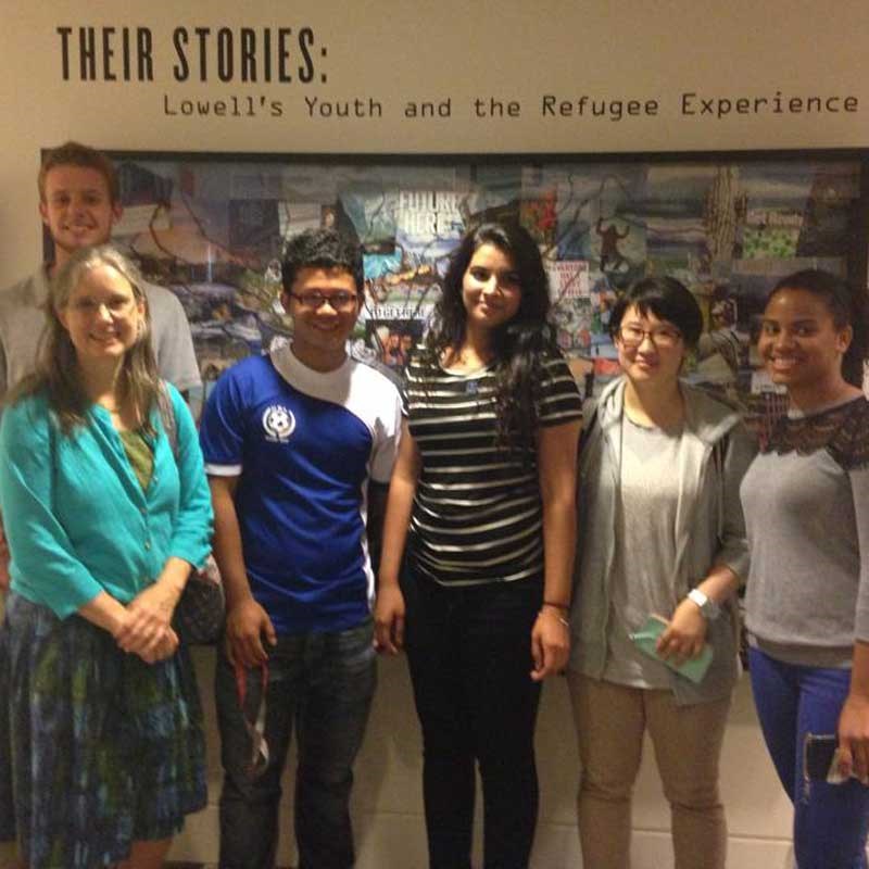 Students in front of a banner that says "Their Stories: Lowell's Youth and the Refugee Experience"