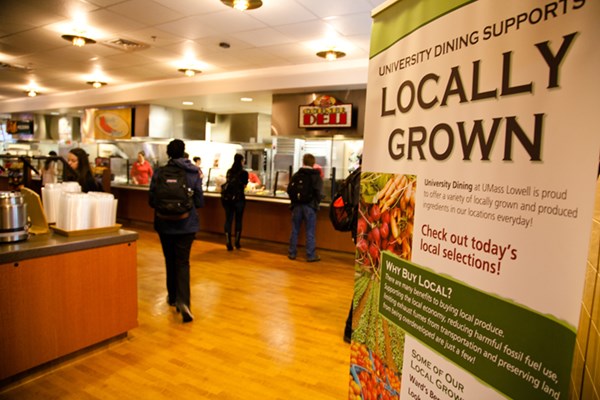 "Locally Grown" sign featuring a list of some of Southwick Dining's locally grown produce, students getting lunch in the background