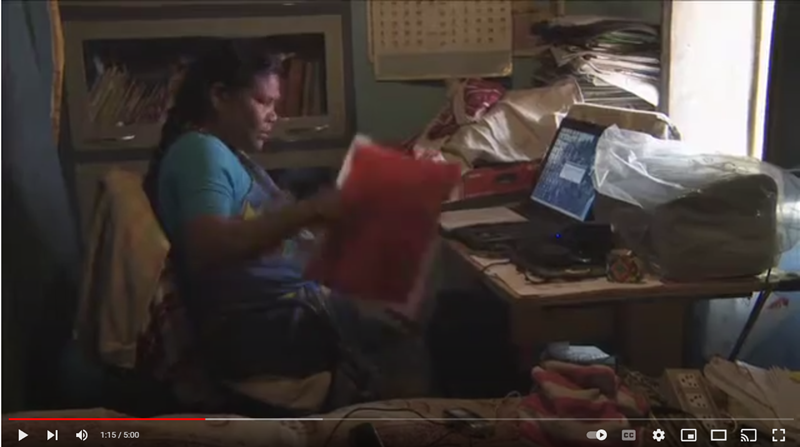 Screenshot from Still I Rise YouTube video showing a woman looking at papers seated at a computer.