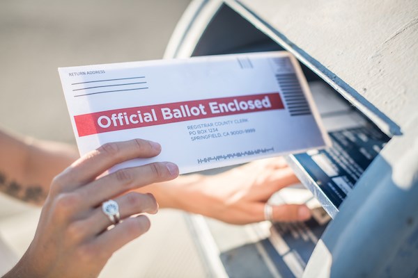 a person drops a mail-in ballot into a mailbox
