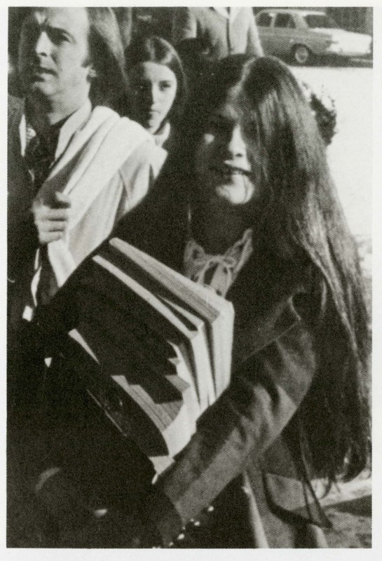 A female student carries a big stack of books to class in 1960