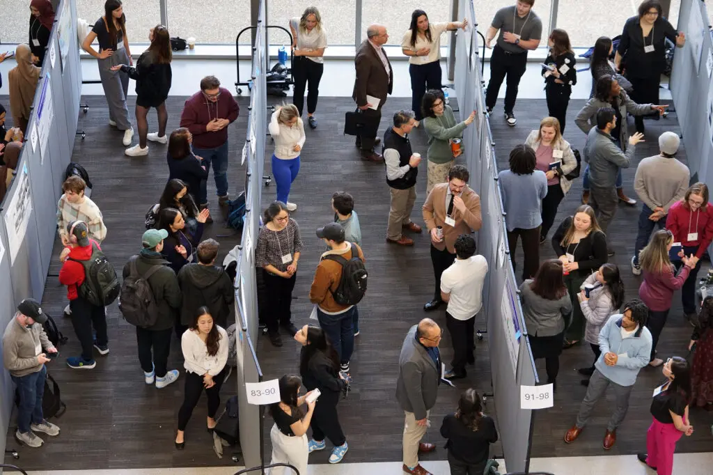 Dozens of students in aisles of student research symposium shot from above