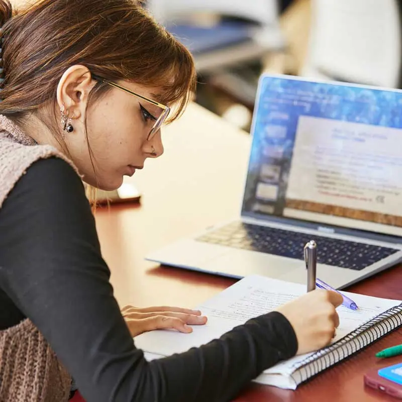 Student writes in a notebook with a laptop nearby