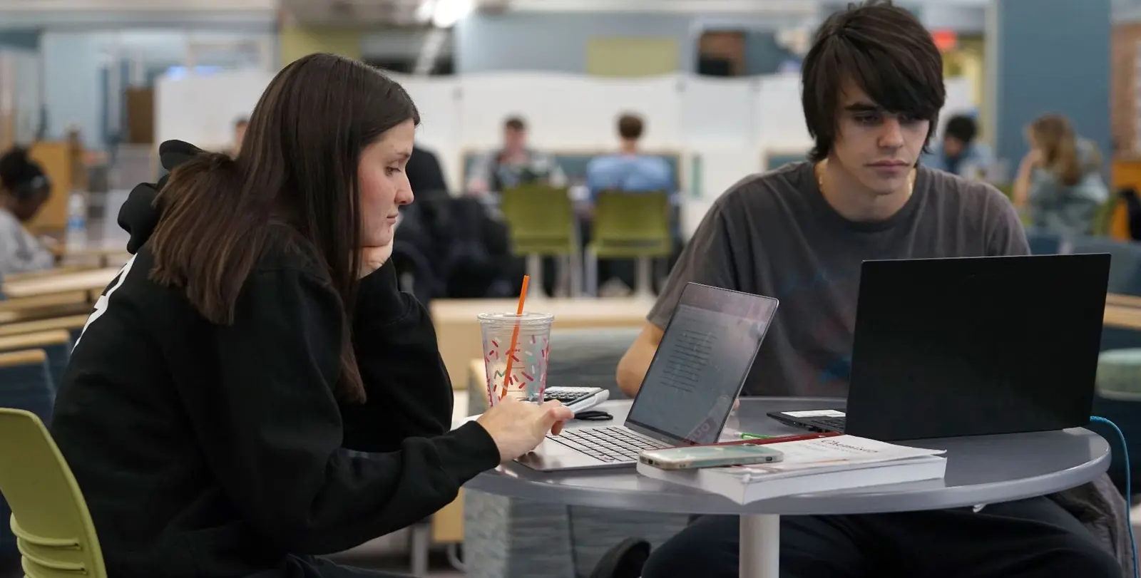 two students share a table working on laptops in library
