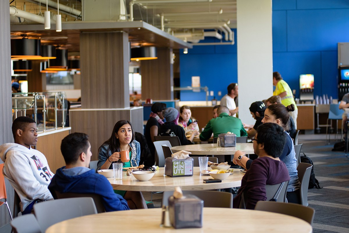 Students eating and talking around a table at the South Campus Dining Commons in the McGauvran Center.