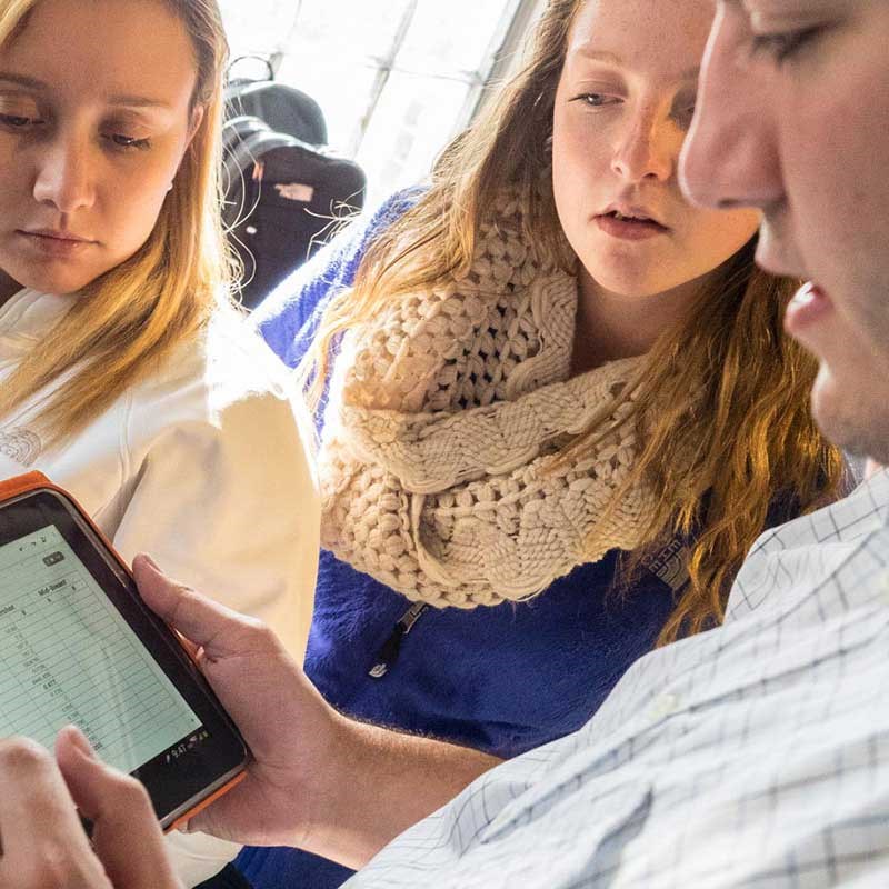 An education student looks at a computer tablet with two middle school students.