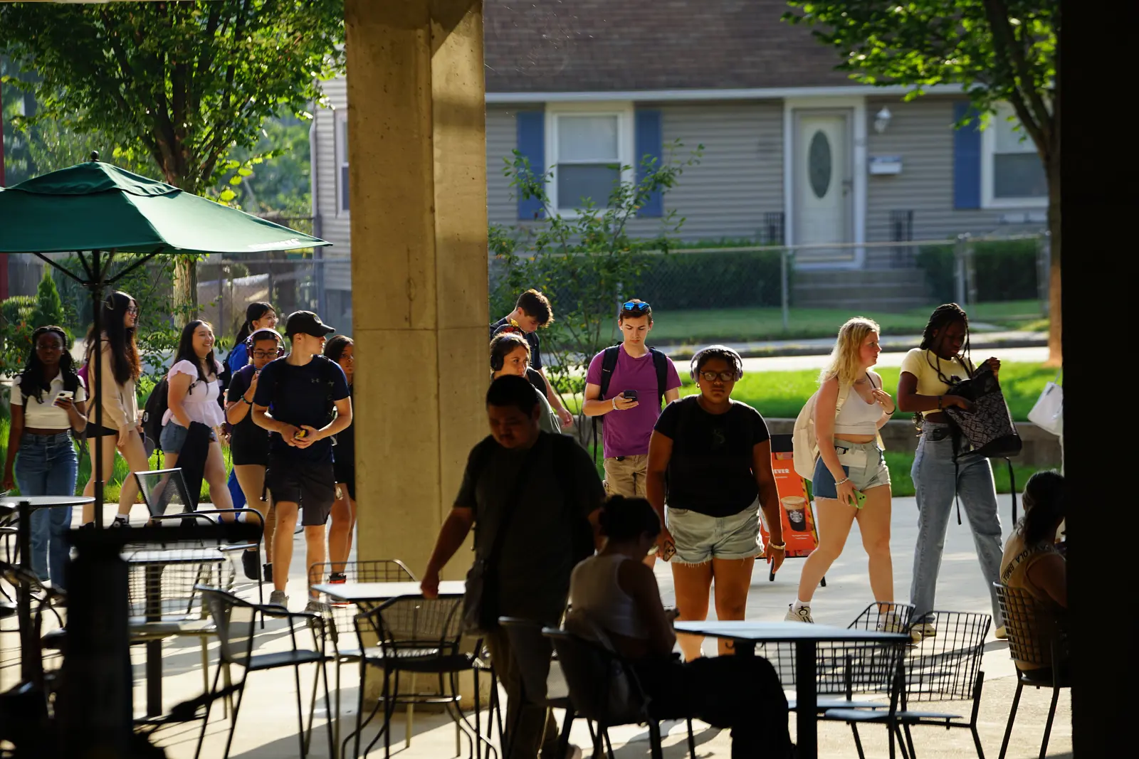 Students with backpacks and carrying books walk through a plaza on a sunny summer day