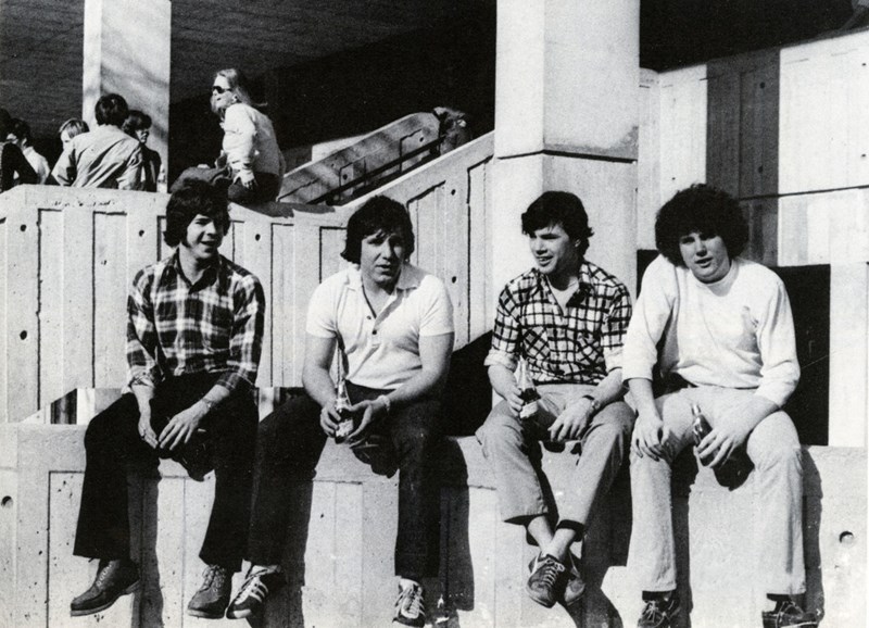 Four male students sit on a wall outside on South Campus in 1977