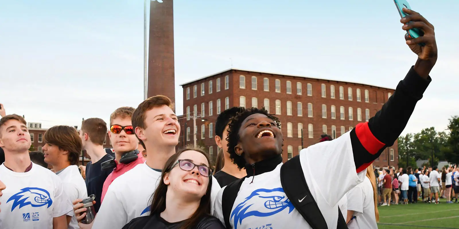 African-American student holding phone taking a selfie of a group on Aiken St. fields