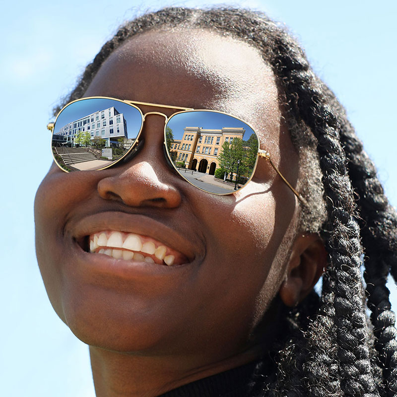 Smiling young black woman with braids and buildings reflected in her sunglasses