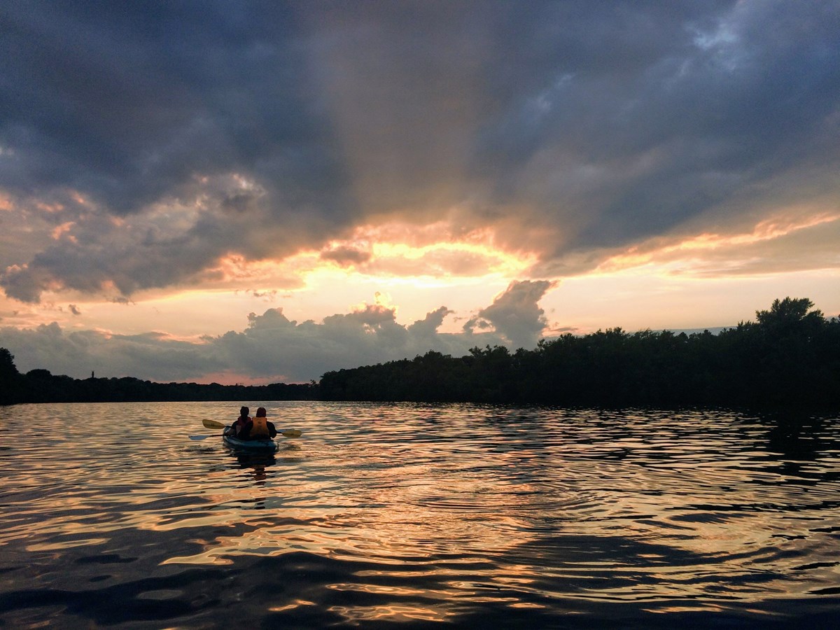a tandem kayak floats in the river watching the sunset with upward rays