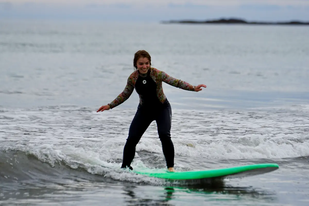 one woman balances on a green surfboard with arms out while she rides a wave